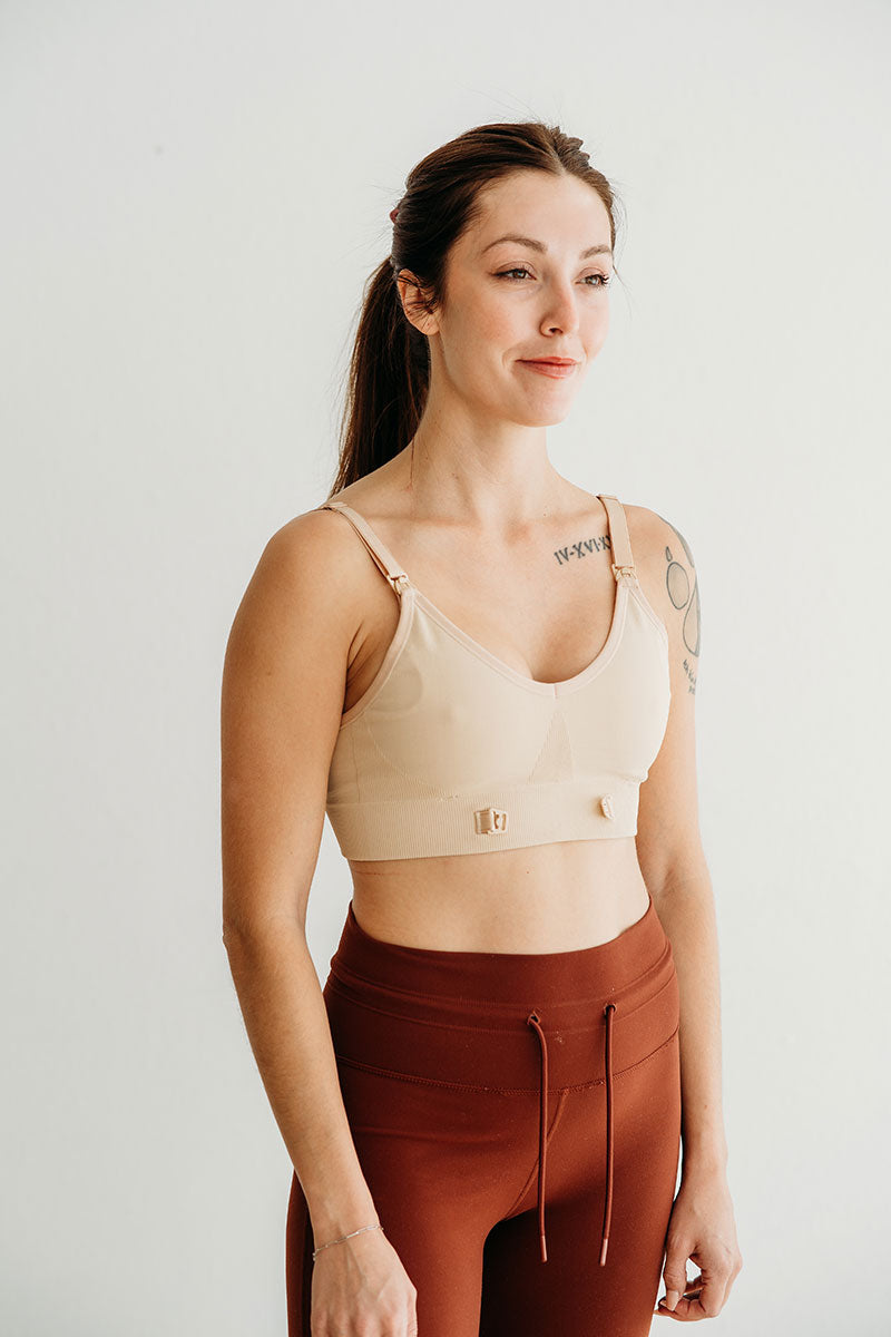 Woman wearing a beige sports bra and brown leggings on a light gray background