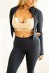 Woman wearing a beige sports bra and black leggings with a black jacket.